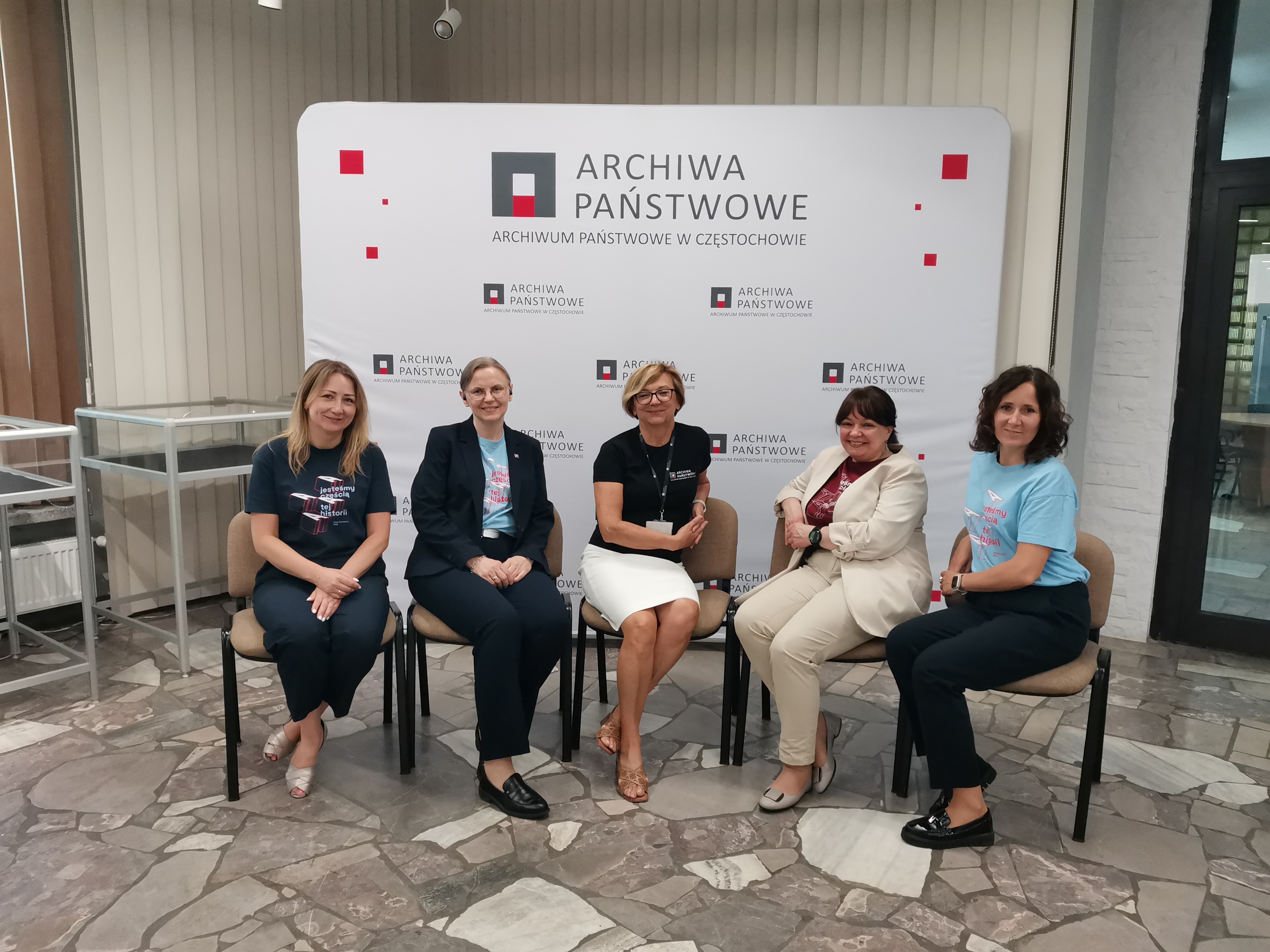 Pięć siedzących na krzesłach kobiet na tle ścianki z logiem Archiwum Państwowego