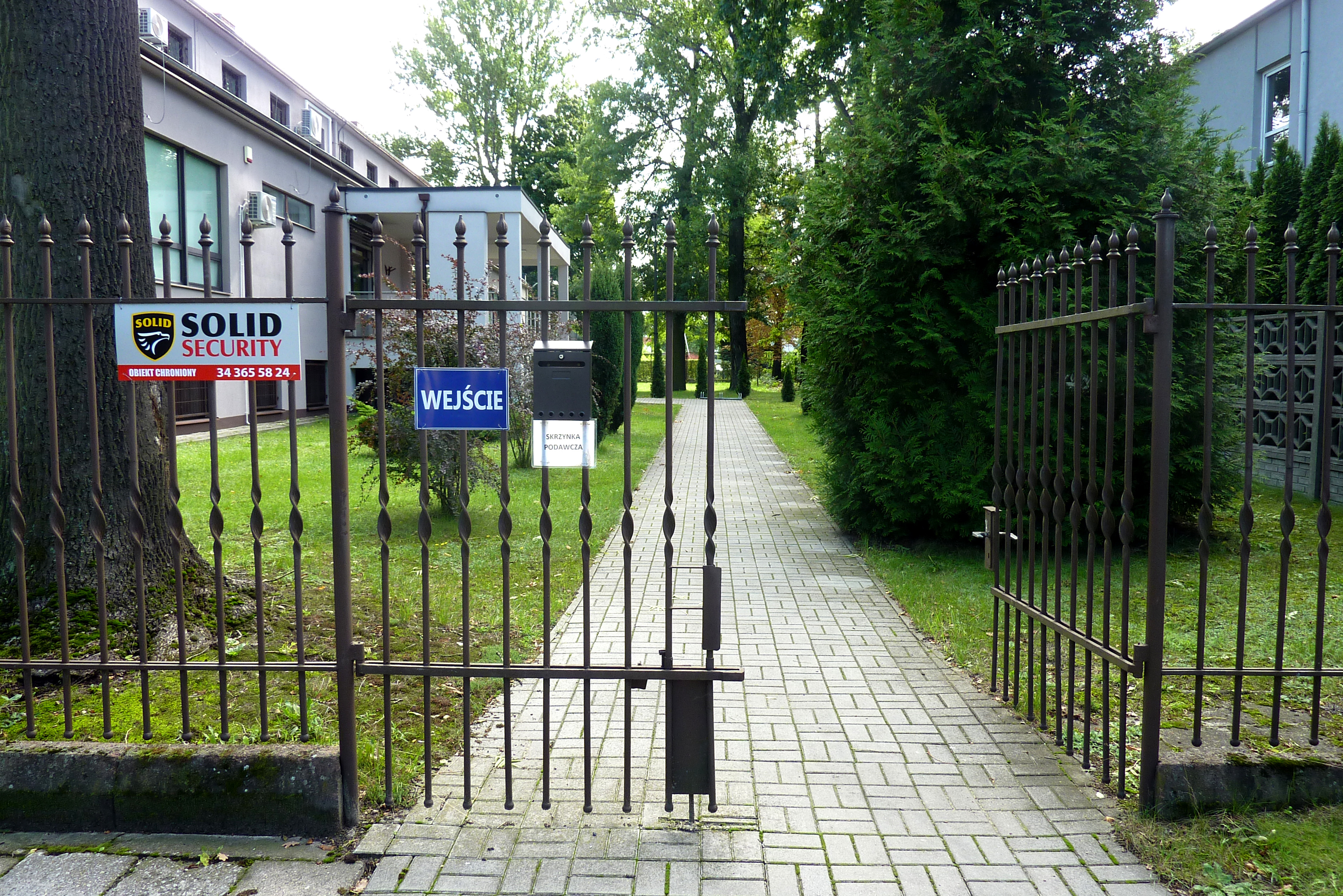 Widok z drogi dojazdowej na furtkę i chodnik prowadzący do wejścia.