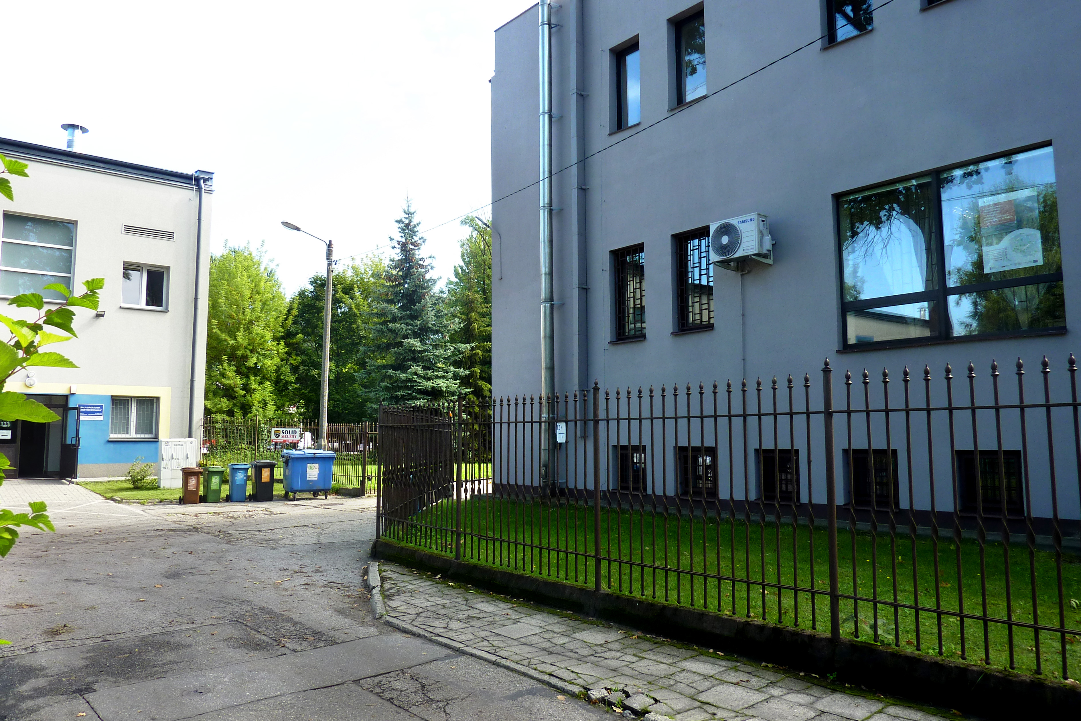 Na prawo od furtki po minięciu budynku Archiwum znajduje się brama wjazdowa na parking.